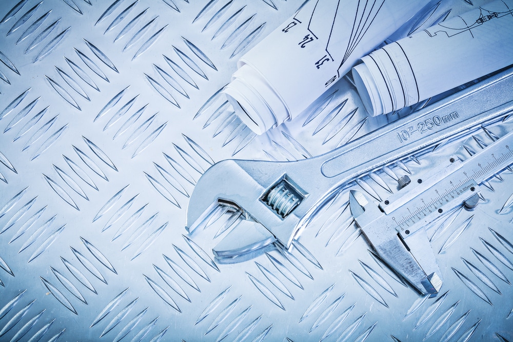 Blueprints vernier caliper adjustable wrench on channeled metal sheet maintenance concept.
