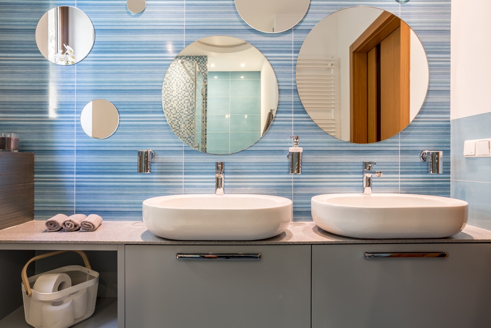 Blue bathroom vanity with two sinks and oval mirrors